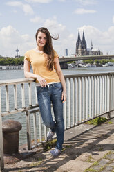 Germany, Cologne, portrait of smiling young woman standing in front of Rhine Rive - FEXF000213