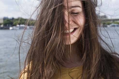 Deutschland, Köln, Porträt einer lächelnden jungen Frau mit wehendem Haar vor dem Rhein - FEXF000214