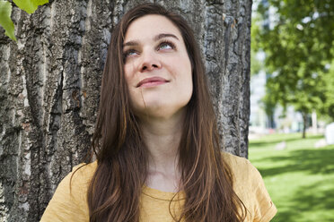 Portrait of young woman sitting in front of tree trunk - FEXF000218