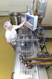 Germany, Saxony-Anhalt, woman operating control of machine in a baking factory, elevated view - LYF000231