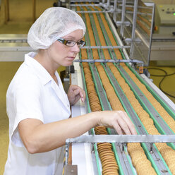 Deutschland, Sachsen-Anhalt, Frau kontrolliert Kekse am Fließband in einer Backfabrik - LYF000239