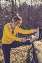 Deutschland, Hessen, Lampertheim, Frau beim Sport im Wald, Stretching auf einem Holzgeländer - UUF001504