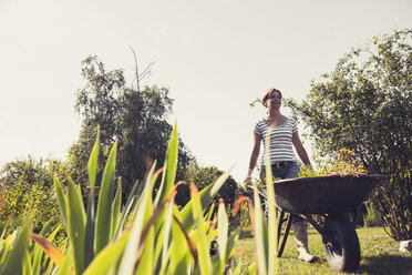 Mature woman pushing wheelbarrow in garden - UUF001470