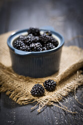 Bowl of blackberries, Rubus sectio Rubus, on jute and dark wood - MAEF008821