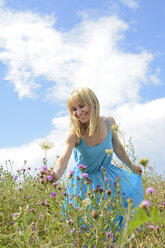 Glückliche junge Frau auf einer Wildblumenwiese beim Pflücken von Blumen - BFRF000483