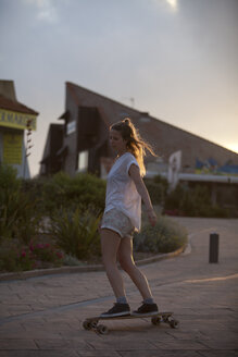 France, Aquitaine, Seignosse, woman longboarding on the street at twilight - FAF000033