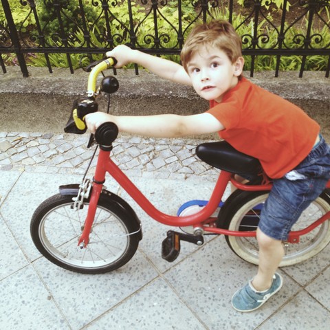 Kleiner Junge sitzt auf einem Fahrrad auf dem Bürgersteig, lizenzfreies Stockfoto