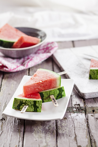 Schale und Teller mit Melonen-Eis am Stiel auf Stoff und Holz, lizenzfreies Stockfoto