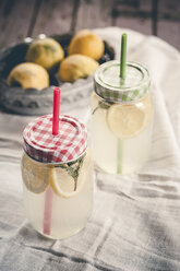 Two screw-top jars of lemon and mint infused water and a bowl of lemons on cloth - SBDF001128