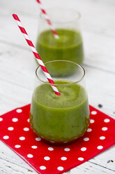 Glass of green smoothie with drinking straw on red-white napkin on white wood - SARF000749