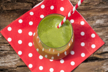 Glass of green smoothie with drinking straw on red-white napkin and bark, elevated view - SARF000750