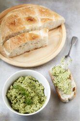 Bowl of pea coriander hummus, slices of flat bread and spoon on metal, elevated view - EVGF000724