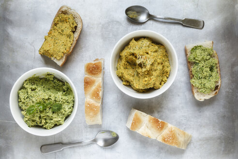 Schalen mit Erbsen-Koriander- und Karotten-Fenchel-Hummus, Scheiben von Fladenbrot und Löffel auf Metall, erhöhter Blick - EVGF000727