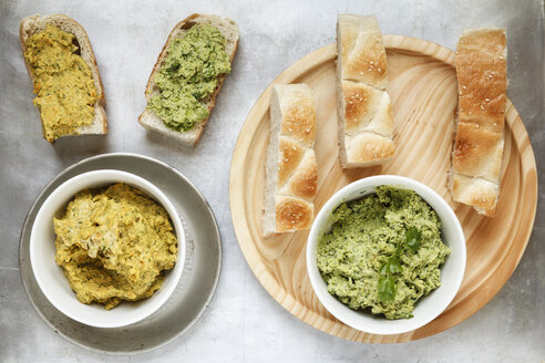 Schalen mit Erbsen-Koriander- und Karotten-Fenchel-Hummus und Fladenbrotscheiben auf Holzbrett und Metall, erhöhter Blick - EVG000731