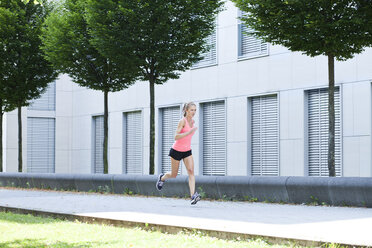 Junge Frau joggt vor der Fassade eines Bürogebäudes - MAEF008875