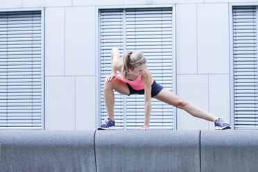 Young woman doing stretching exercise in front of facade of an office building - MAEF008877