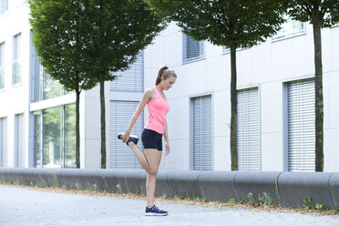 Young woman doing stretching exercise in front of facade of an office building - MAEF008885