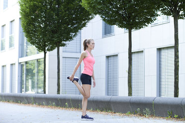 Young woman doing stretching exercise in front of facade of an office building - MAEF008886