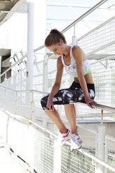 Young woman wearing sportswear sitting on a railing of pedestrian bridge - MAEF008895