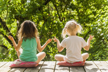 Two relaxed girls sitting on wooden terrace - TCF004210