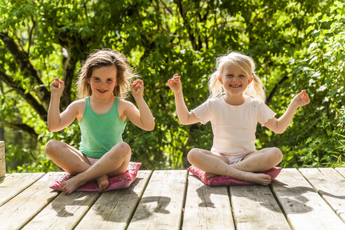 Two smiling girls sitting on wooden terrace - TCF004211