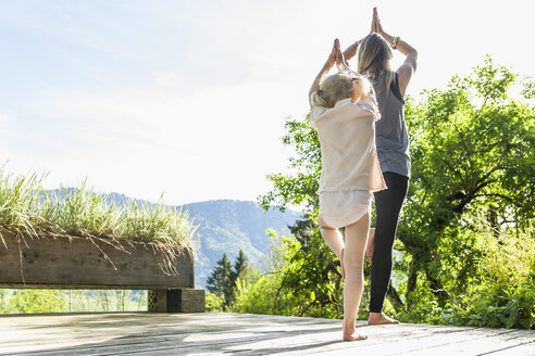 Mother and daughter practicing yoga on wooden terrace - TCF004167