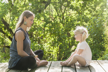 Mother and daughter sitting opposite on wooden terrace - TCF004215