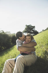 Vater, der seine lachende kleine Tochter auf einer Wiese umarmt - UUF001586