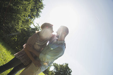 Laughing young couple standing on a meadow at back light - UUF001552