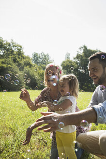 Parents and little daughter making soap bubbles on a meadow - UUF001527