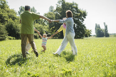 Drei Generationen Familie spielen Ringelreihen auf einer Wiese - UUF001539