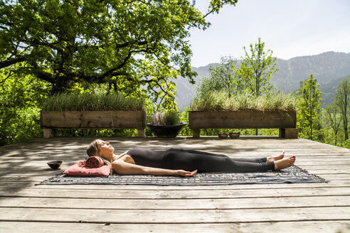 Woman lying on wooden terrace meditating - TCF004132