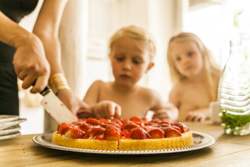 Woman dividing strawberry cake for two girls - TCF004206