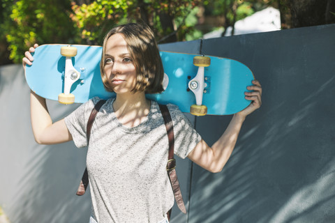 Porträt einer jungen Skateboarderin mit Skateboard auf den Schultern, lizenzfreies Stockfoto