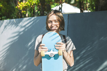 Porträt einer lächelnden jungen Skateboarderin, die ihr Skateboard hält - EBSF000272