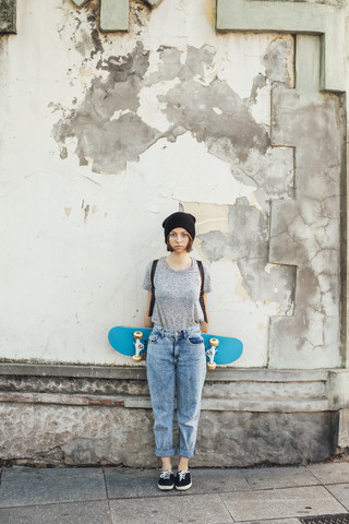 Porträt einer ernst dreinblickenden jungen Skateboarderin vor einer Fassade, lizenzfreies Stockfoto
