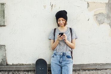 Portrait of smiling young female skate boarder using smartphone - EBSF000279