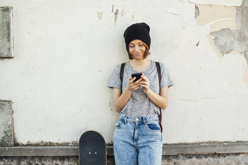 Porträt einer lächelnden jungen Skateboarderin mit Smartphone - EBSF000279