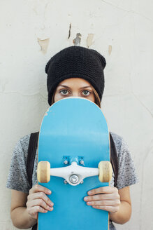 Portrait of young female skate boarder holding hiding behind her skateboard - EBSF000283