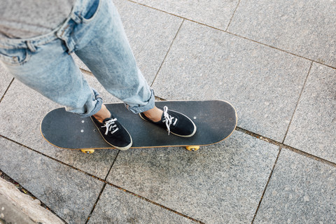 Junge Skateboarderin steht auf ihrem Skateboard, Teilansicht, lizenzfreies Stockfoto