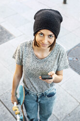 Porträt einer lächelnden jungen Skateboarderin, die ein Smartphone und ein Skateboard hält, Blick von oben - EBSF000298