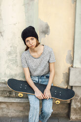 Porträt einer jungen Skateboarderin mit ihrem Skateboard vor einer Fassade - EBSF000295