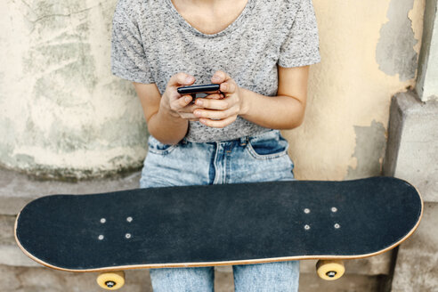 Junge Skateboarderin mit Smartphone und Skateboard vor einer Fassade, Teilansicht - EBSF000297