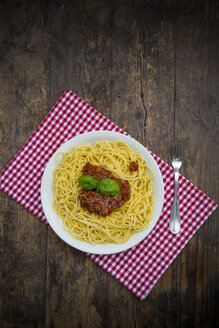 Teller mit Spaghetti Bolognese, Gabel und Tuch auf dunklem Holz, Ansicht von oben - LVF001754