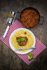 Teller mit Spaghetti Bolognese, Kochtopf mit Bolognesesoße, Parmesan, Reibe und Tuch auf dunklem Holz, Ansicht von oben - LVF001736