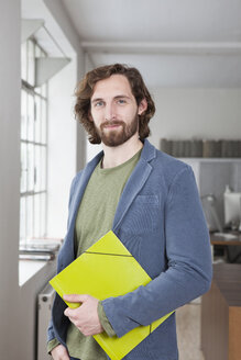 Portrait of smiling young man with file standing in an office - RBF001700