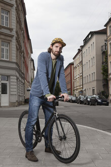 Germany, Bavaria, Munich, young man wearing basecap standing on pavement with his racing cycle - RBF001701