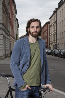 Germany, Bavaria, Munich, portrait of smiling young man standing on pavement with his racing cycle - RBF001704