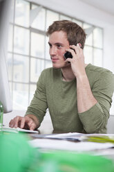 Porträt eines jungen Mannes, der mit seinem Smartphone im Büro telefoniert - RBF001708