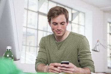 Portrait of young man using his smartphone in the office - RBF001709